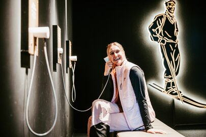 Person telefoniert mit Wandapparat im Retro-Stil und lacht dabei.