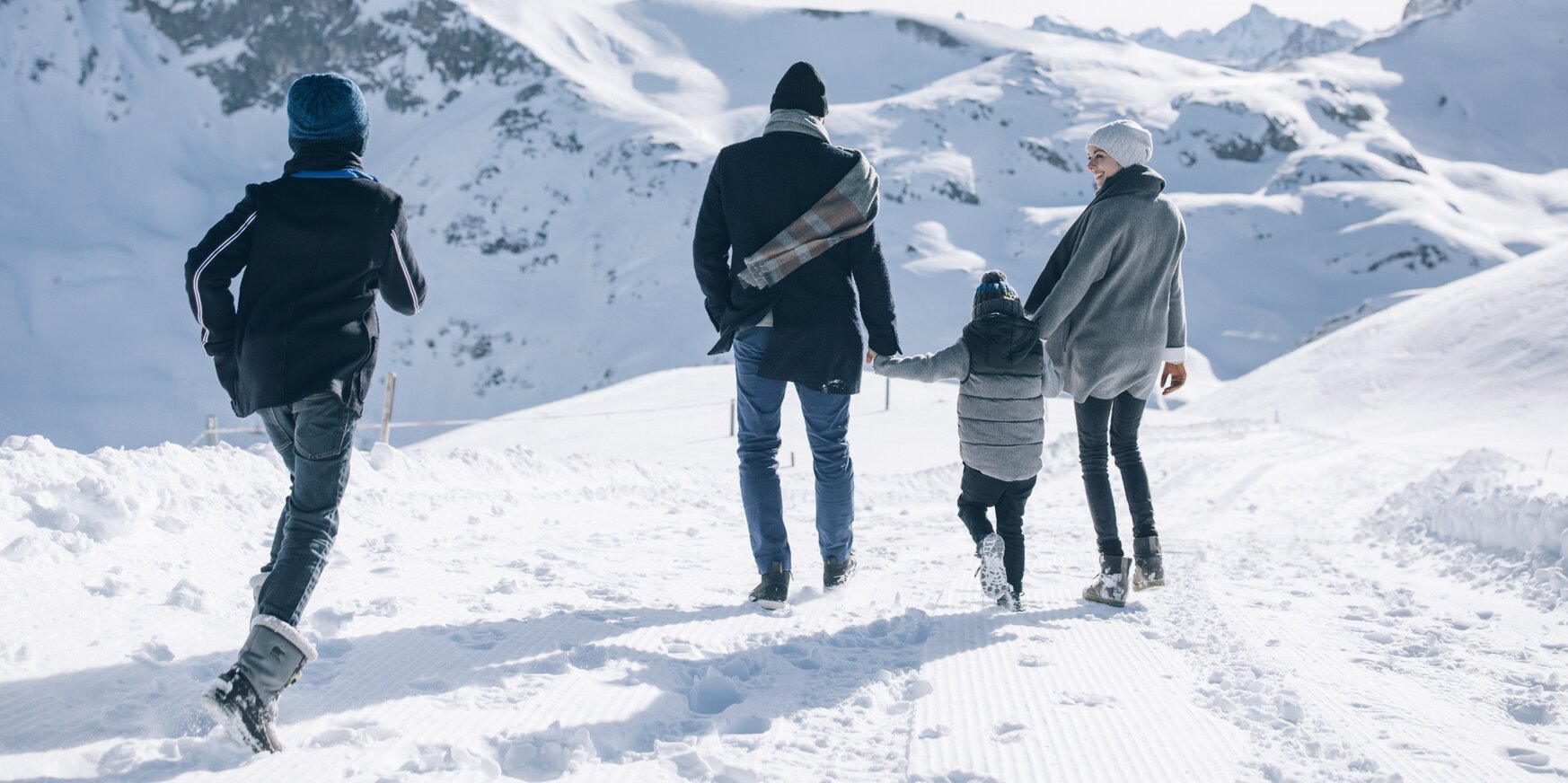 Familie spaziert im Schnee in einer bergigen Winterlandschaft.