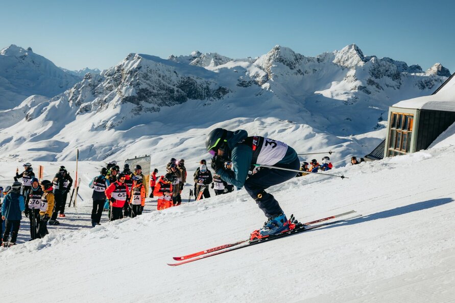 Skifahrer startet beim Weißen Ring-Rennen, Zuschauer und verschneite Berge im Hintergrund.