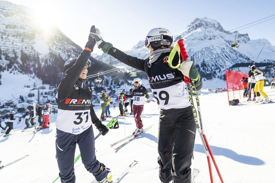 Zwei Skifahrer bei 'Der Weiße Ring' klatschen sich auf der Piste ab. Berglandschaft im Hintergrund.