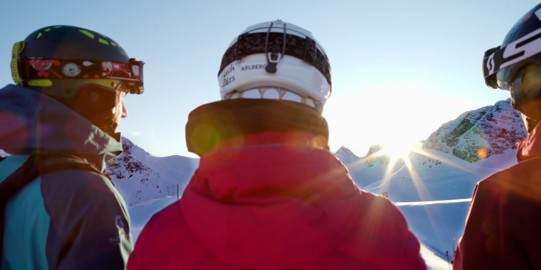 Drei Skifahrer blicken zum Sonnenaufgang in den Bergen.