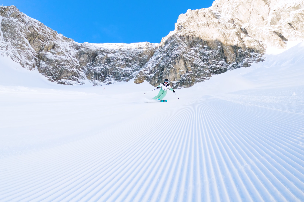 Skifahrer auf frisch präparierter Piste, umgeben von Bergen.