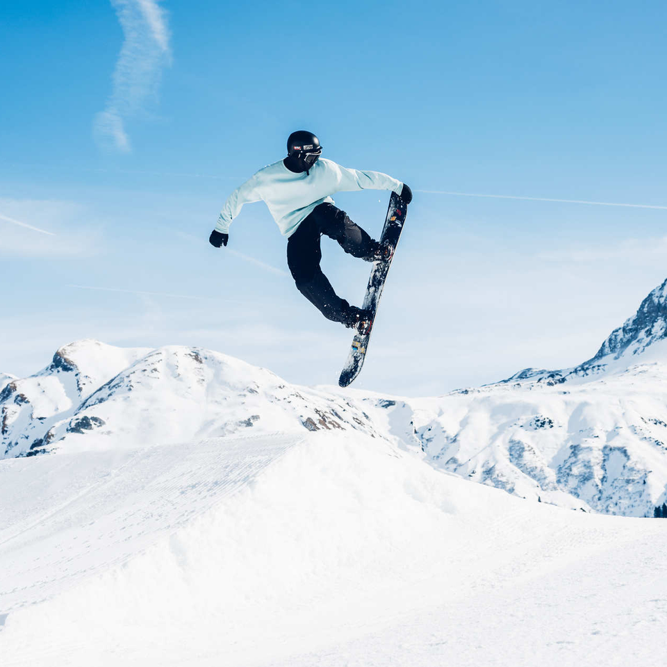 Snowboard macht vor einer Kulisse aus schneebedeckten Bergen einen Sprung.