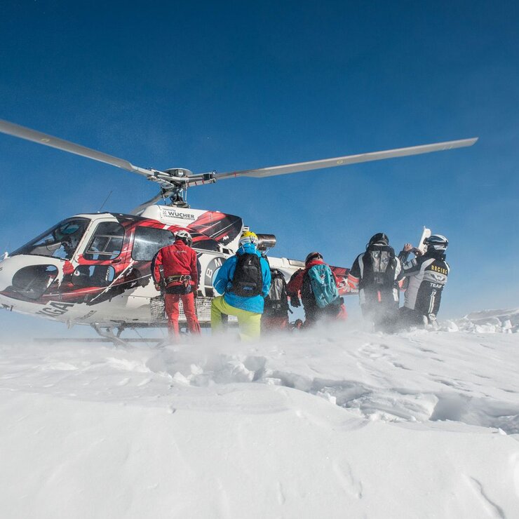 Personen steigen aus einem Hubschrauber auf einem verschneiten Berg aus.