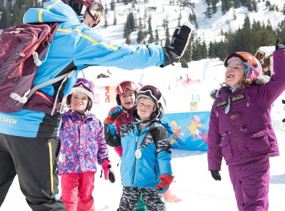 Kinder in Skibekleidung geben ihrer Skilehrerin ein High-Five.