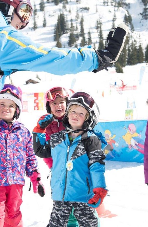 Kinder in Skibekleidung geben ihrer Skilehrerin ein High-Five.