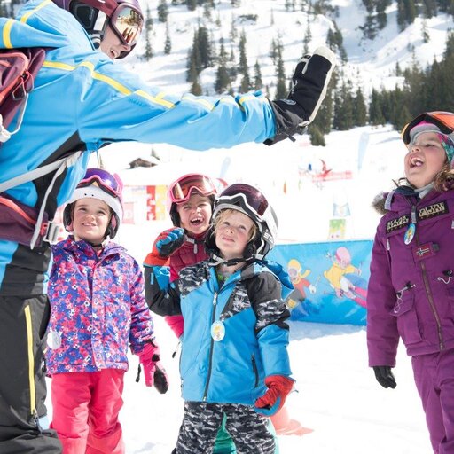 Kinder in Skibekleidung geben ihrer Skilehrerin ein High-Five.