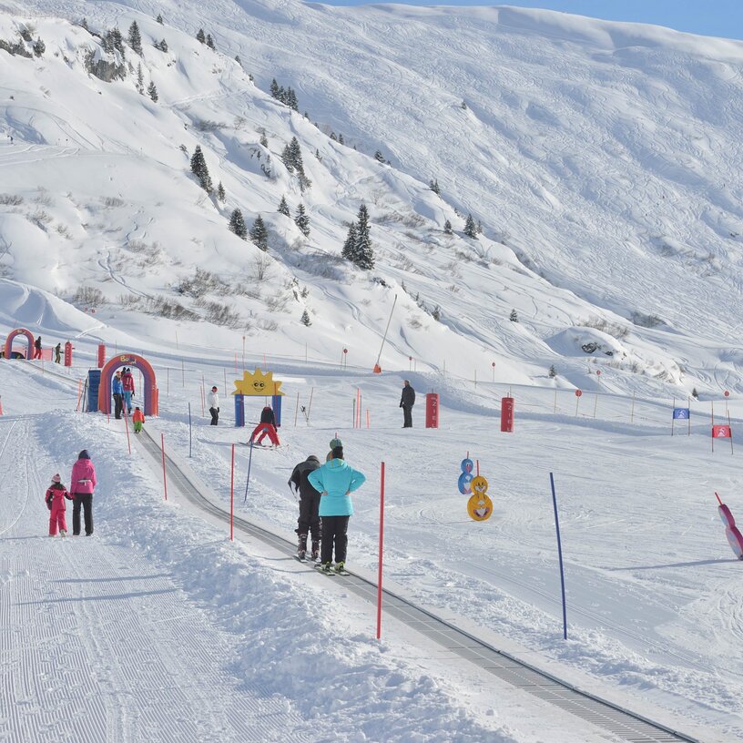 Familien genießen Skifahren und Snowboarden auf einer Anfängerpiste im Kinderland Zürs.