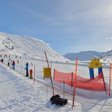 Kinder lernen in sonniger Winterlandschaft Ski zu fahren.