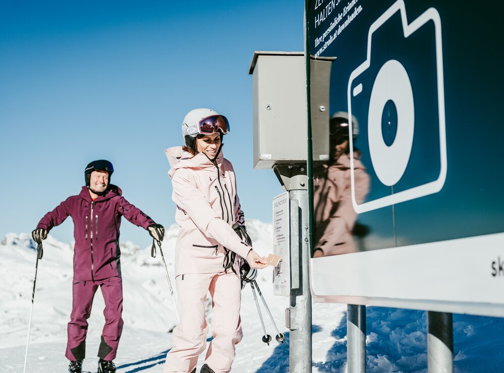 Zwei Skifahrer machen an einer Fotostation neben der Piste ein Foto.