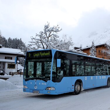 Ein blauer Ortsbus fährt durch eine verschneite Ortschaft von Lech Zürs.