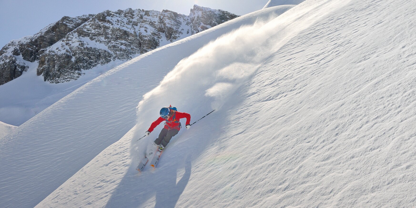 Skifahrer meistert eine steile Piste bei Sonnenschein und Pulverschnee.