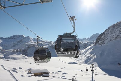 Seilbahn mit Logo von "Skiregion Lech Zürs" vor verschneitem Bergpanorama.