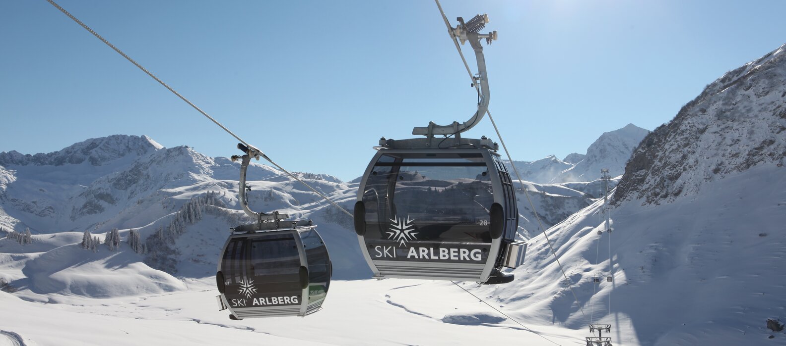 Seilbahn mit Logo von "Skiregion Lech Zürs" vor verschneitem Bergpanorama.