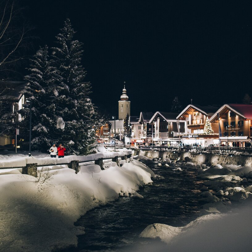 Verschneite Stadt und Fluss bei Nacht in der Skiregion Lech Zürs.