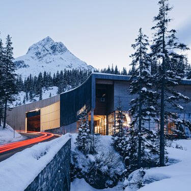 Modernes Heizwerk der Skiregion Arlberg inmitten einer schneebedeckten Landschaft, durch die eine Autostraße führt. 