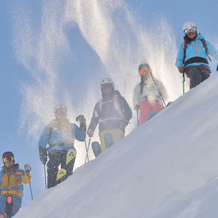 Gruppe von Skischülern auf einem verschneiten Hang bei Sonnenschein.