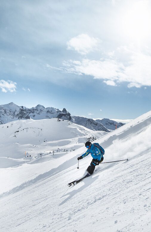 Zwei Skifahrer sausen bei Sonnenschein die Piste hinunter.