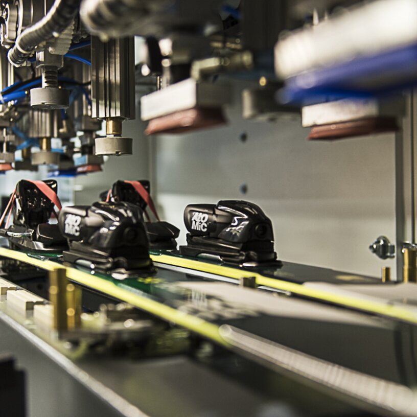 Nahaufnahme eines automatisierten Skimontageprozesses mit Bindungen auf Skiern.