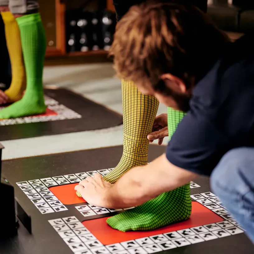 Person mit gemusterten Socken wird für einen 3D-Scan des Fußes vorbereitet.