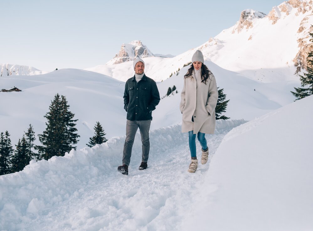 Paar spaziert im Schnee durch eine verschneite Landschaft.