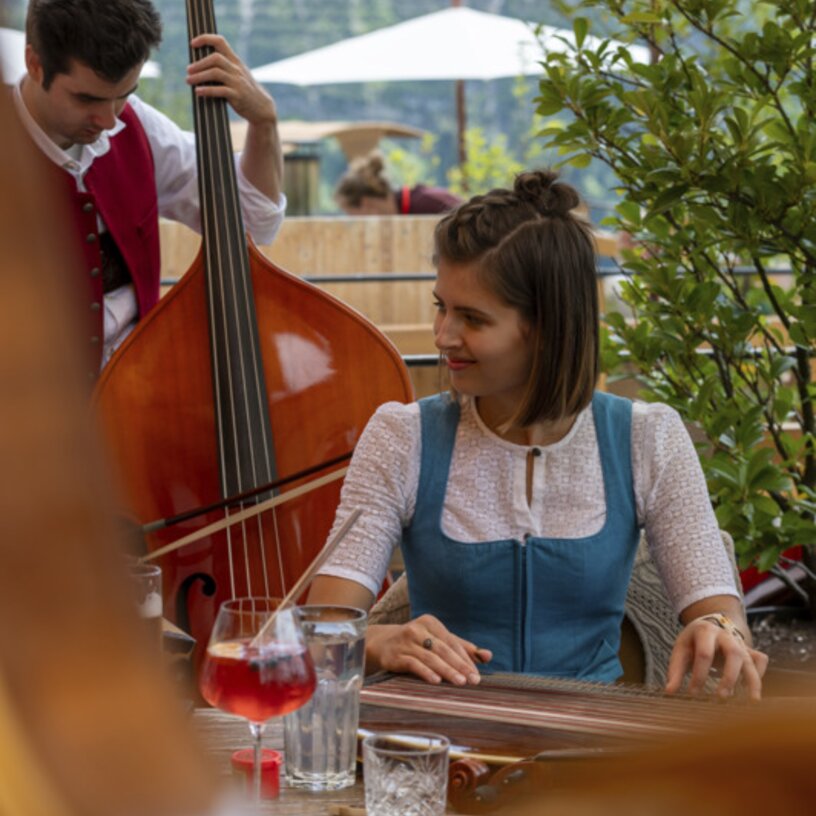 Frau in traditioneller Kleidung spielt Zither, daneben steht ein Bassist.