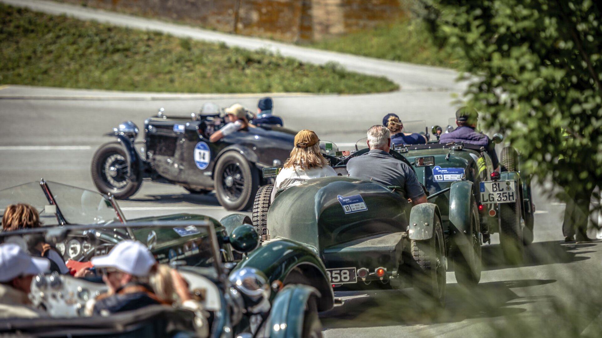 Mehrere Oldtimer auf einer Straße bei einer Ausfahrt. Fahrer und Beifahrer genießen die Fahrt unter freiem Himmel.