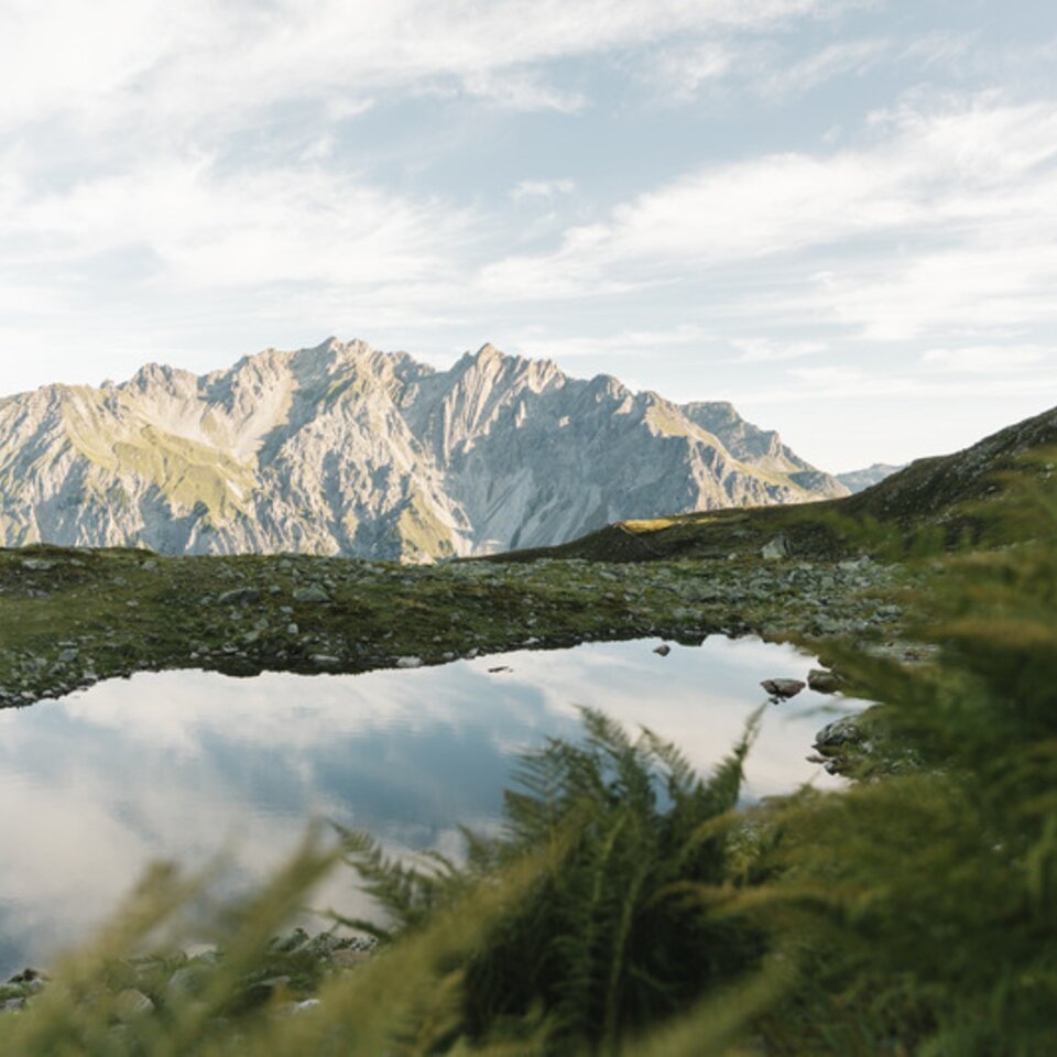 Ein kleiner Bergsee spiegelt felsige Berggipfel unter klarem Himmel wider.