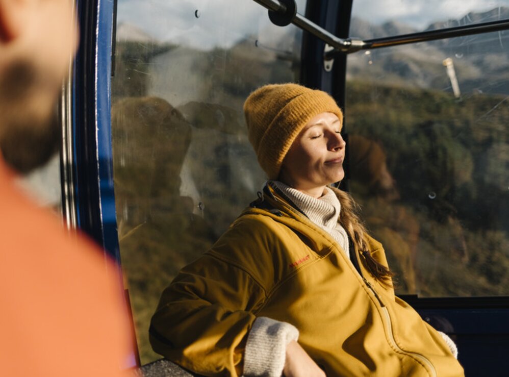 Person entspannt sich in Seilbahn bei Sonnenschein.