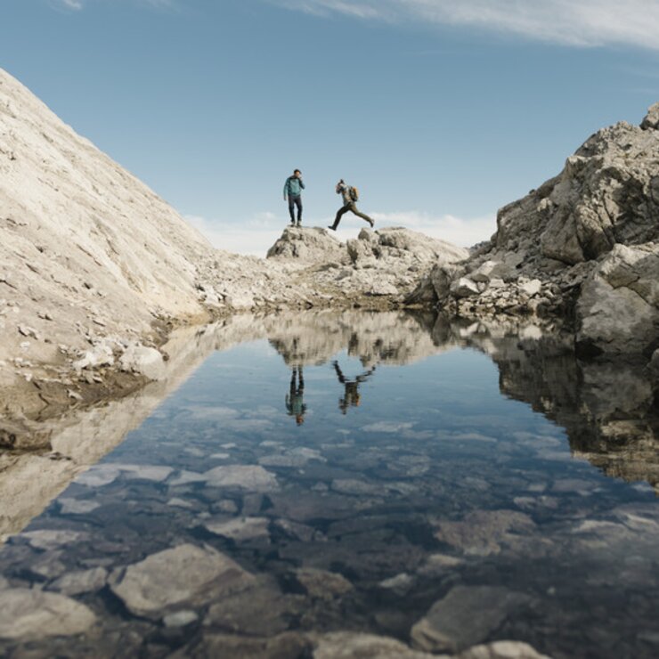 Zwei Personen wandern über Felsformationen spiegeln sich dabei im Wasser.