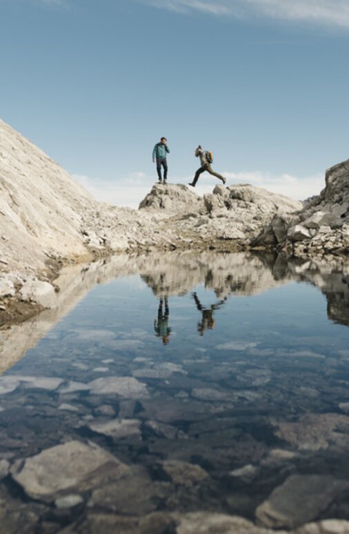 Zwei Personen wandern über Felsformationen spiegeln sich dabei im Wasser.