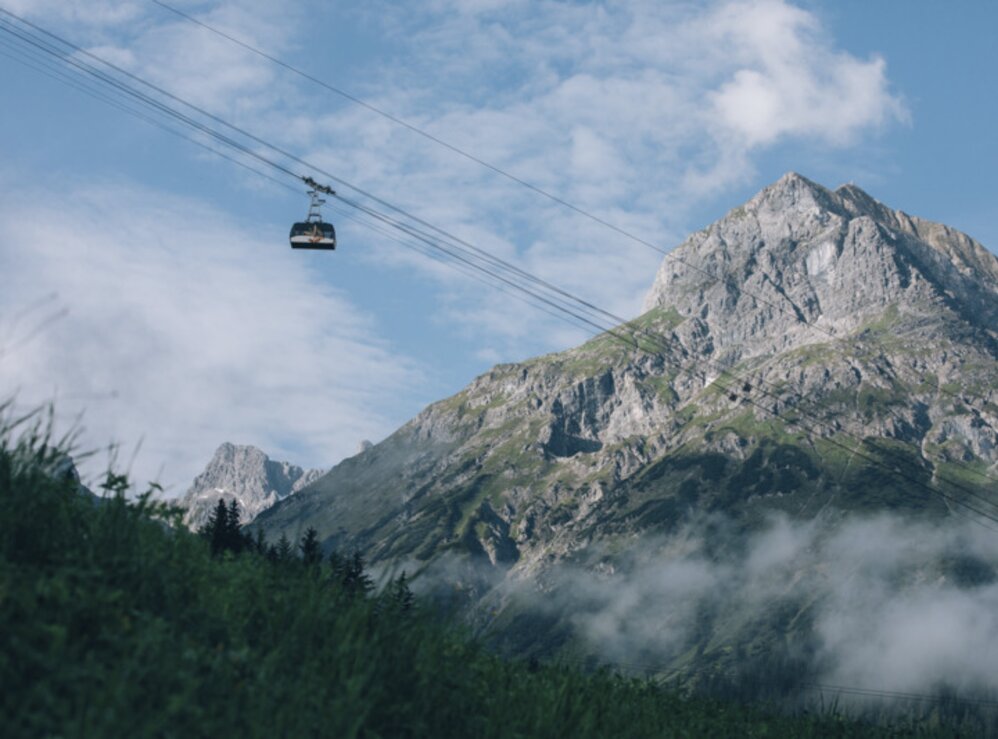 Seilbahn schwebt vor einem imposanten Bergmassiv.