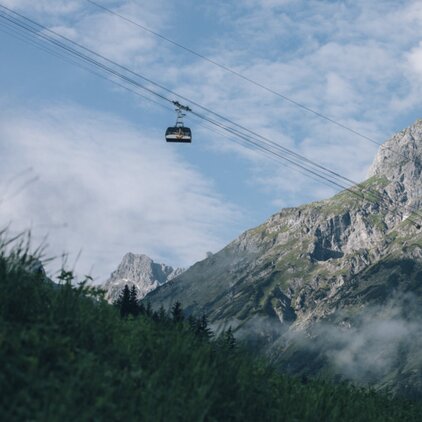 Seilbahn schwebt vor einem imposanten Bergmassiv.