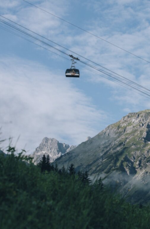 Seilbahn schwebt vor einem imposanten Bergmassiv.