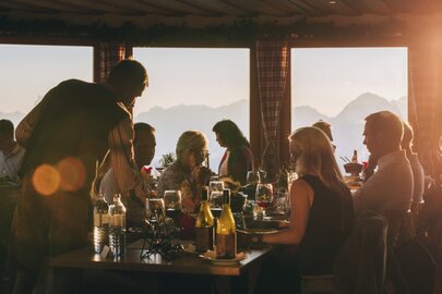 Menschen sitzen an einem Tisch, trinken Wein und genießen den Sonnenuntergang.