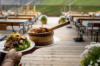 Ein Salat und ein Gröstl werden auf einer Terrasse einer Berghütte im Sommer serviert.