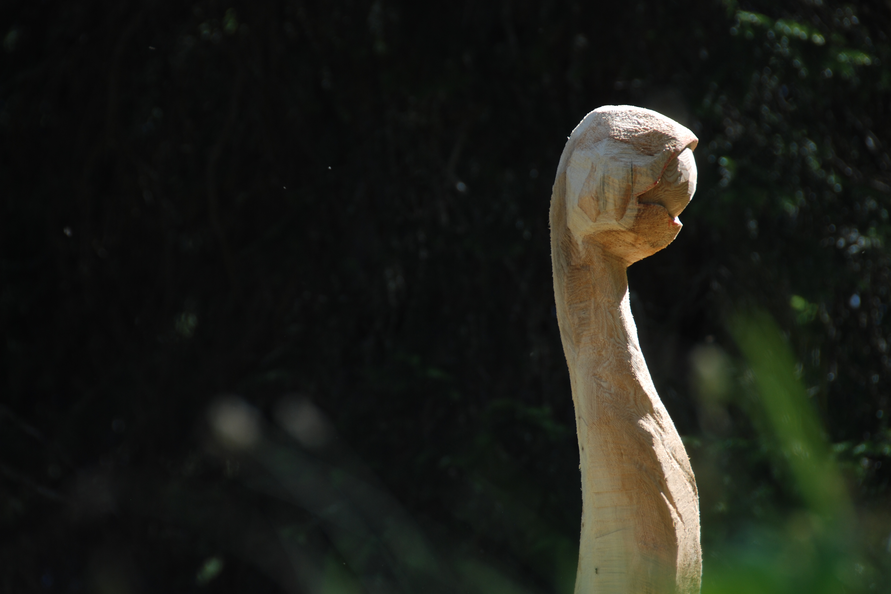 Eine geschnitzte Holzfigur, die einem erhobenen Arm ähnelt, ragt in das Waldlicht der Umgebung.