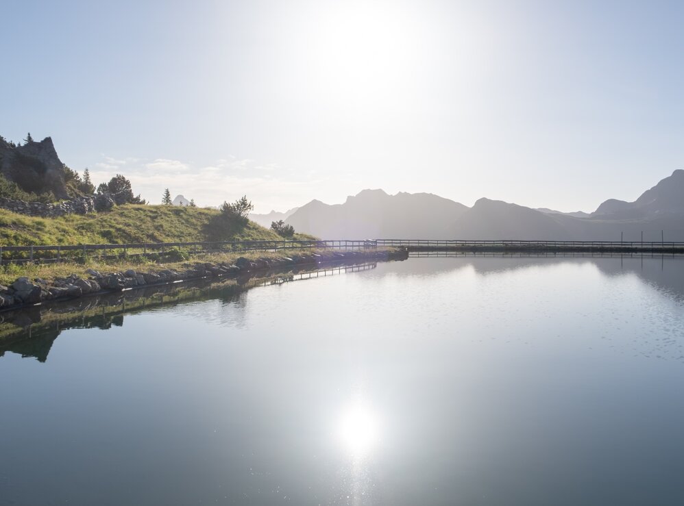 Eine ruhige Seelandschaft mit Lichtreflexionen und Bergblick.