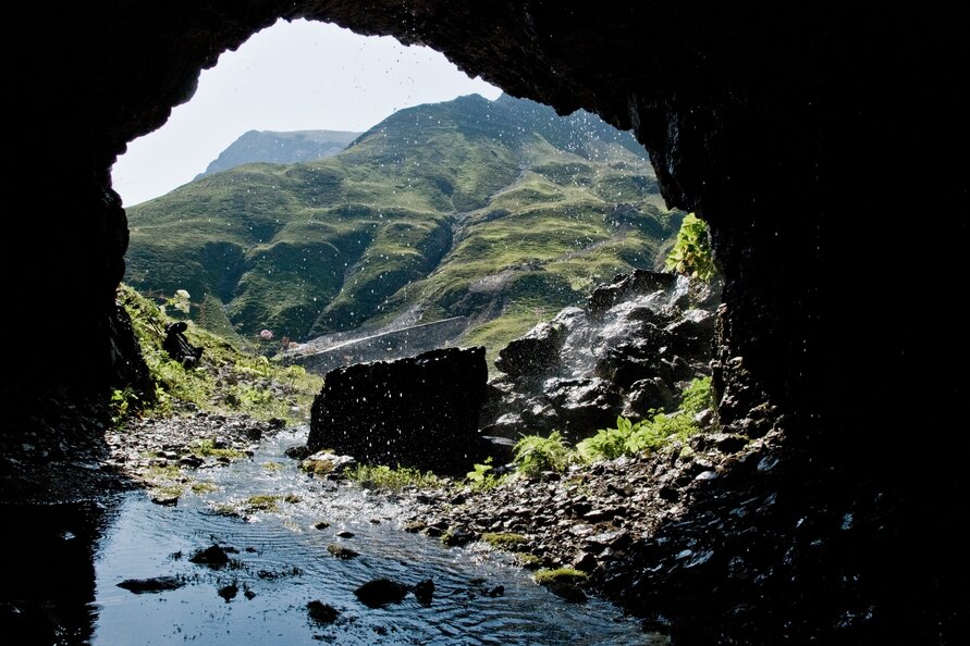 Blick aus einer Höhle auf die grüne Berglandschaft.