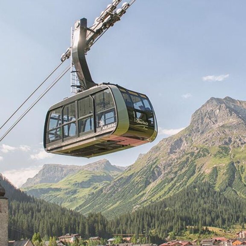 Eine Seilbahn fährt über ein Tal in Richtung des Familienbergs Kriegerhorn mit malerischen Bergen im Hintergrund.