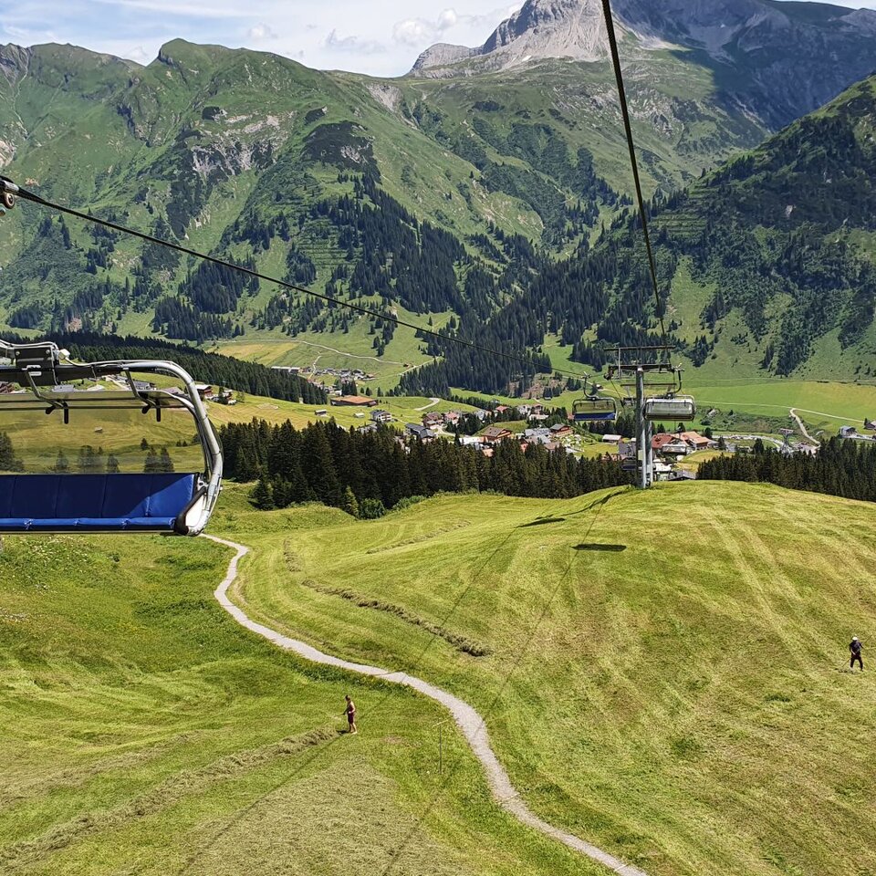 Sessellift über grünen Hügeln mit Ausblick auf das Kriegerhorn und ein Dorf im Hintergrund.