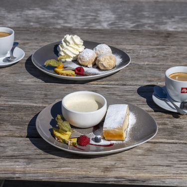 Kaffee mit Dessertteller, Sahne, Obst und Gebäck auf Holztisch.
