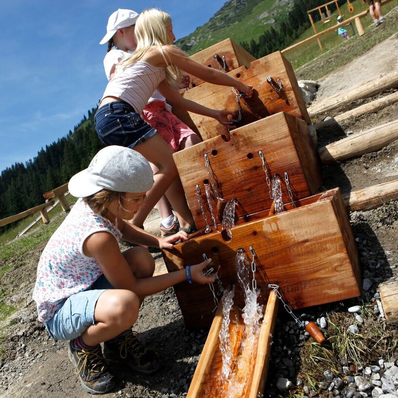 Kinder spielen mit Wasser in Holzrinnen am Wasserspielplatz auf dem Familienberg Kriegerhorn.