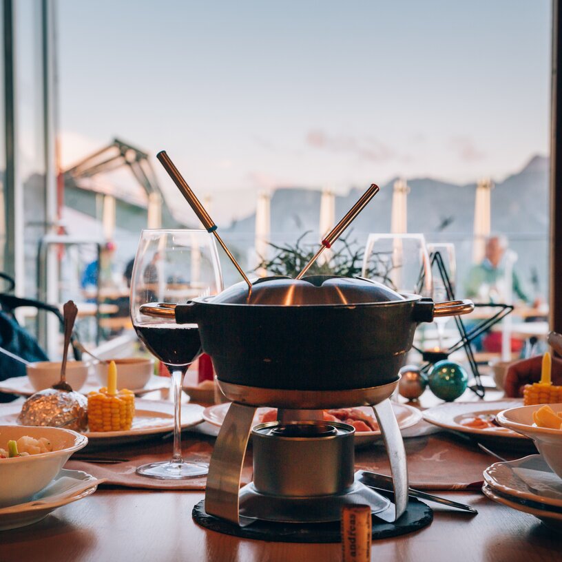 Ein Tisch mit Käsefondue, Wein und Beilagen im Panoramarestaurant Rüfikopf.
