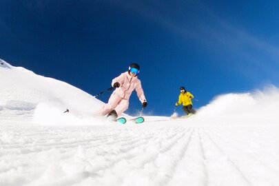 Two skiers in colorful suits skiing down a snowy slope.