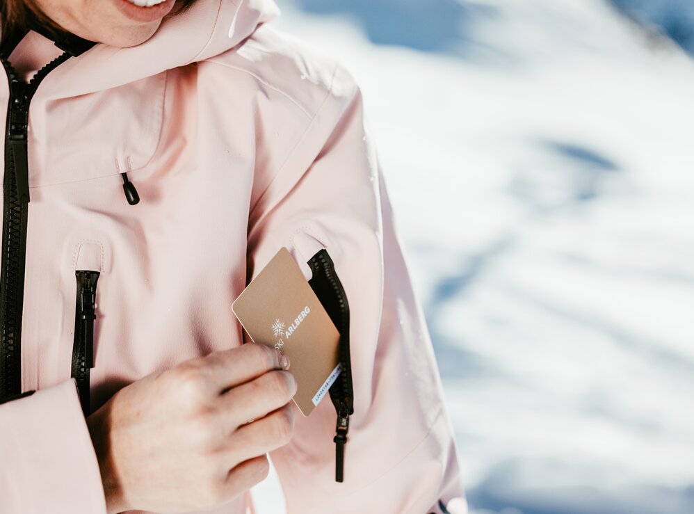 Person steckt ihren Skipass von Ski Arlberg in die Ärmeltasche ihrer rosa Jacke. 
