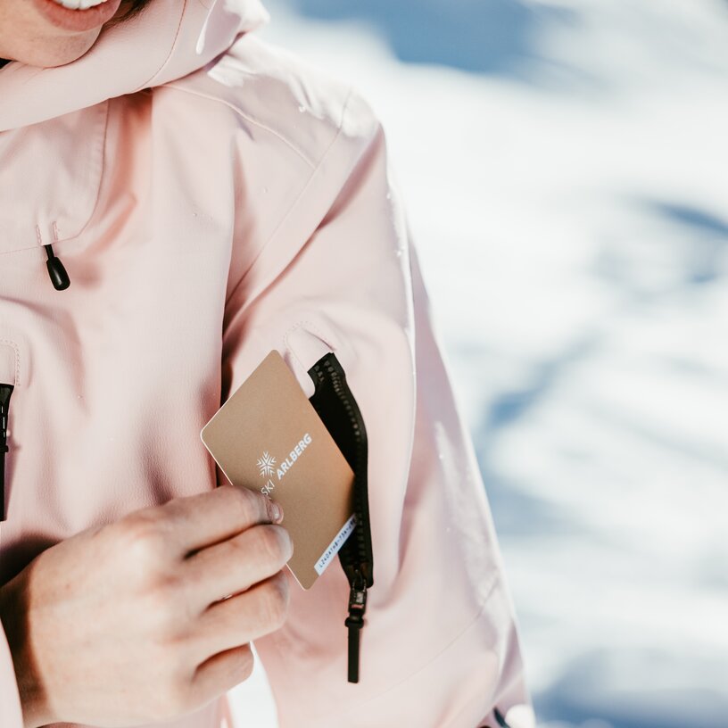 Person steckt ihren Skipass von Ski Arlberg in die Ärmeltasche ihrer rosa Jacke. 