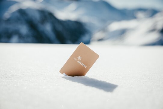 Ein goldener Skipass mit der Aufschrift 'Ski Arlberg' steckt im Schnee.