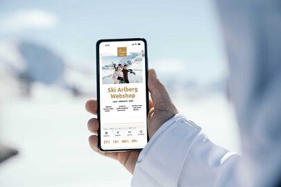 Person hält Handy mit geöffneter Ski Arlberg Webshop-Seite im Schnee.