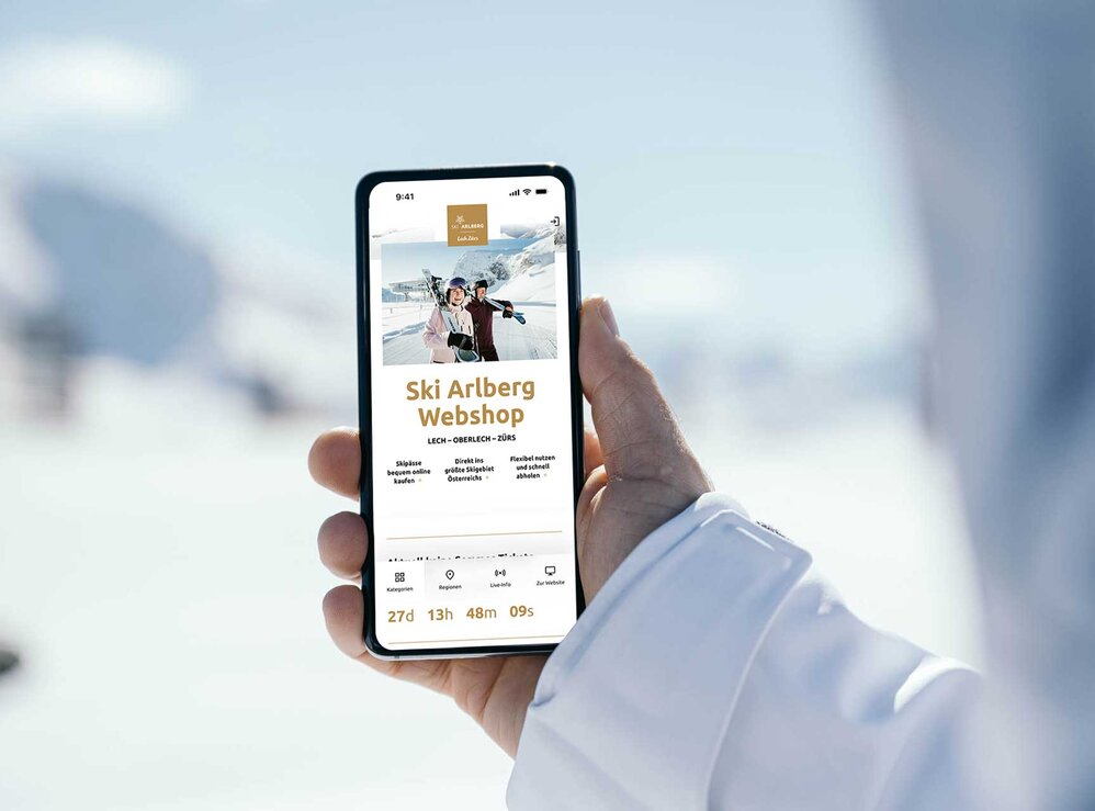 Person hält Handy mit geöffneter Ski Arlberg Webshop-Seite im Schnee.